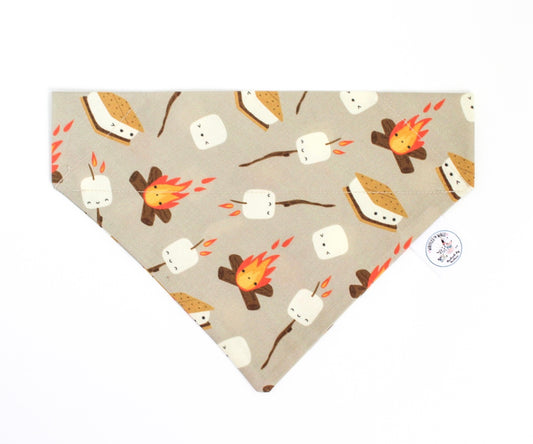 An over the collar pet bandana with a cozy campfire and s'mores print on a light gray background. The pattern features marshmallows, graham cracker s'mores, and small campfires in brown, orange, and white.