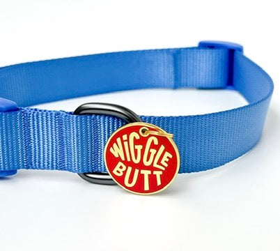 A blue nylon dog collar with a black metal buckle and a circular red and gold tag that reads 'WIGGLE BUTT' in yellow lettering, shown on a white background.