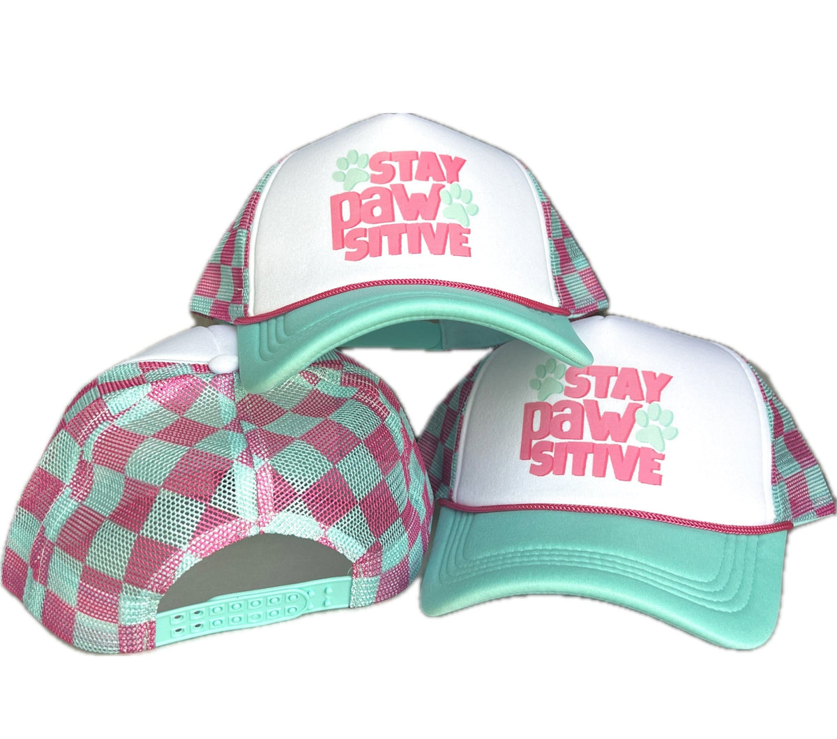 Three views of a trucker hat with a pink and mint green checkered pattern, white front panels, and a mint green brim. The front panel features the text 'STAY PAW SITIVE' in pink with a mint green paw print.