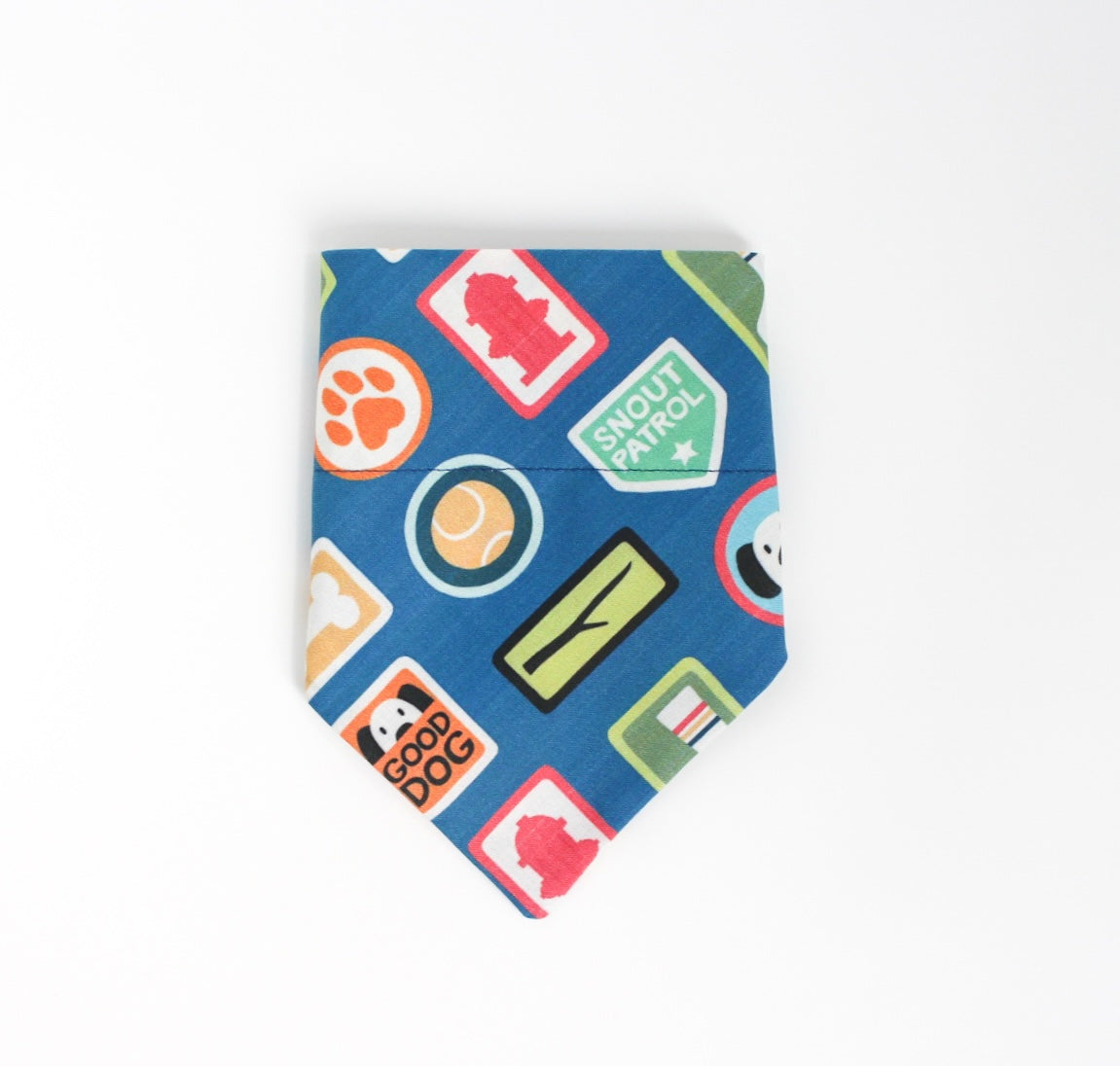 A blue pet bandana featuring a colorful pattern of dog-themed patches and badges, including a paw print, tennis ball, fire hydrant, and 'Snout Patrol' emblem, shown on a plain white background.
