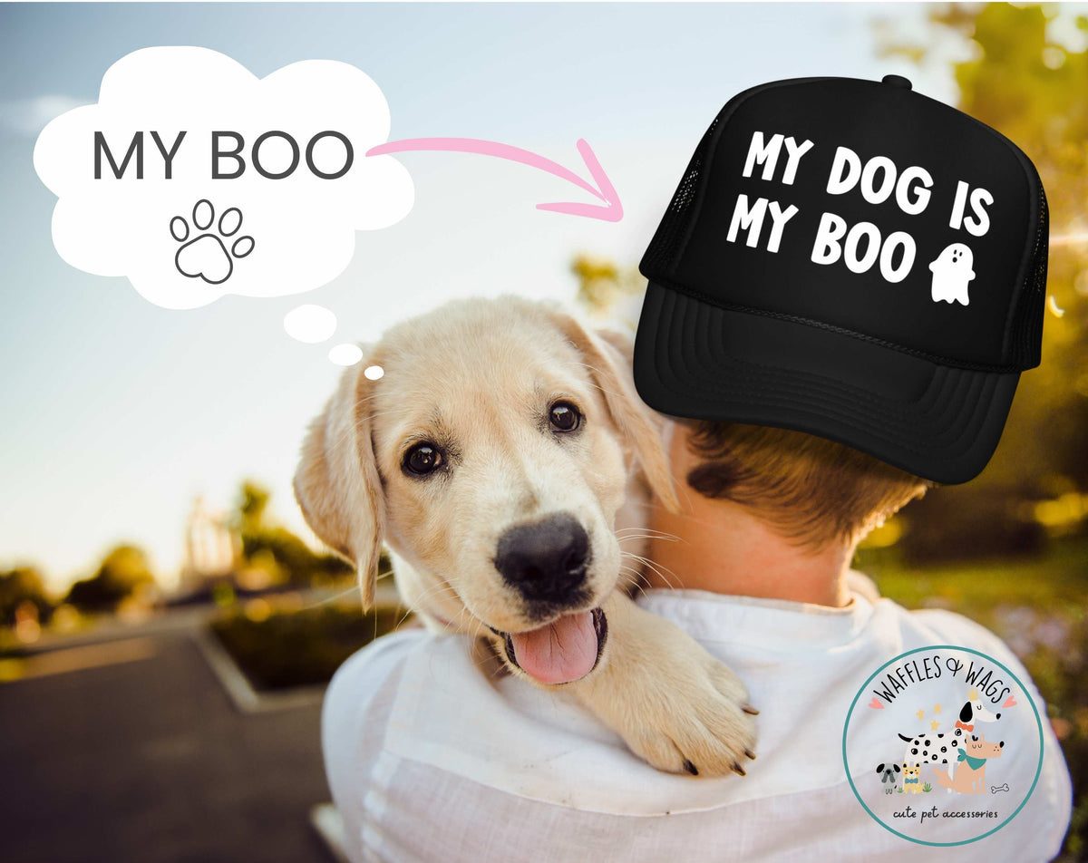 A person outdoors wearing a black trucker hat with the white text 'MY DOG IS MY BOO' and a cartoon ghost, while carrying a light-colored puppy on their shoulder. A thought bubble with a paw print and the words 'MY BOO' appears on the left, and a 'Waffles of Wags' logo is visible on the bottom right.