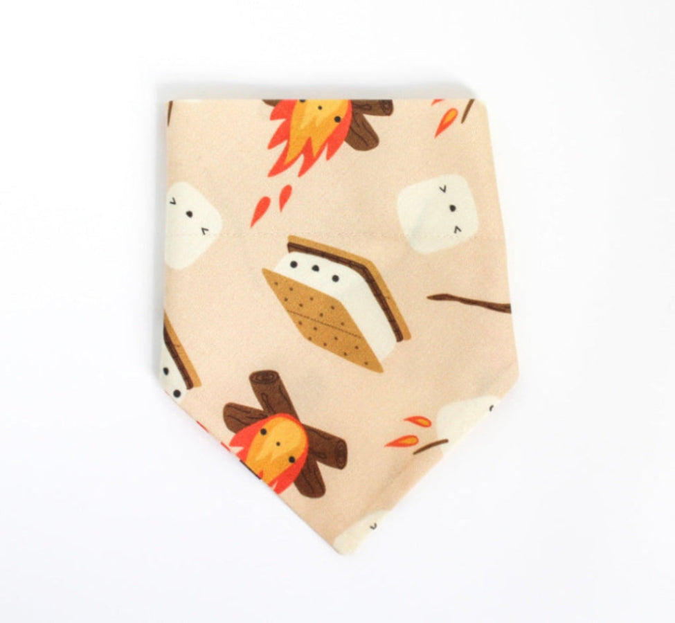 A light peach over the collar bandana-style pet collar featuring a cute cartoon s'mores print with marshmallows, campfires, and a s'mores sandwich, shown on a plain white background.