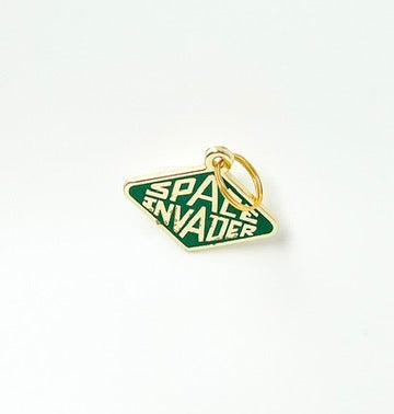 A small enamel pin shaped like a green and white 'Space Invader' diamond sign with gold-tone metal trim and a gold ring attachment, shown on a plain white background.
