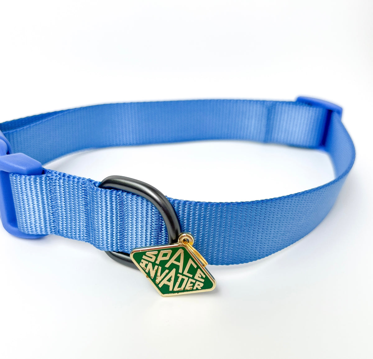 A blue nylon pet collar with a black metal ring and a green diamond-shaped enamel charm that reads 'SPACE INVADER' in gold lettering, shown on a white background.