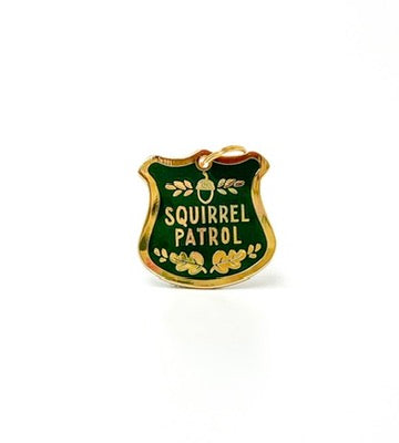 A small enamel-style badge or charm shaped like a police shield, with a gold border, dark green center, and gold text reading 'SQUIRREL PATROL' on a white background.