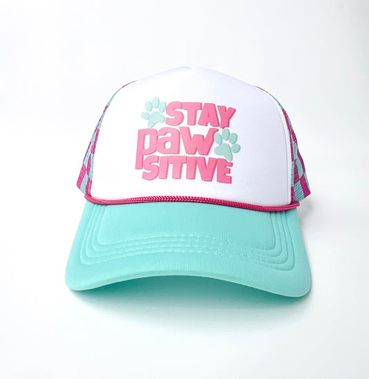 A trucker-style cap with a white front panel, mint green brim, and pink and mint graphic text reading 'STAY PAW SITIVE' with paw prints, shown on a white background.