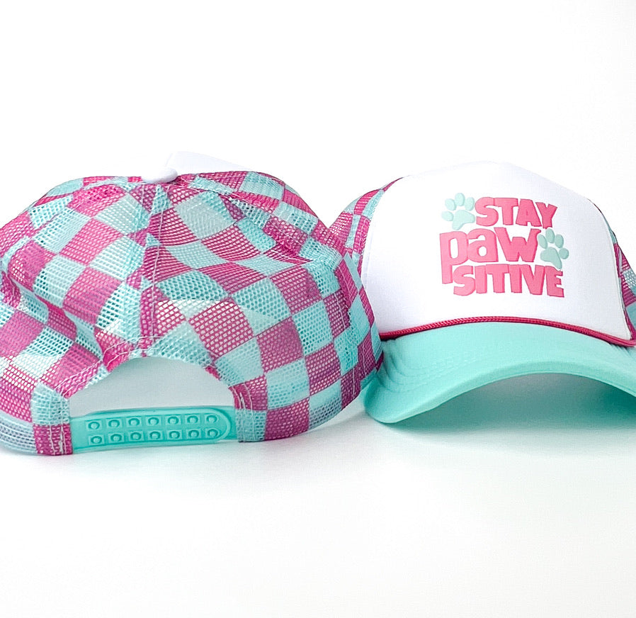 A trucker-style cap with a white front panel, mint green brim, and pink and mint graphic text reading 'STAY PAW SITIVE' with paw prints, shown on a white background.