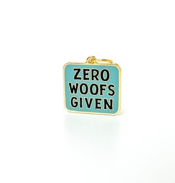 A small rectangular enamel charm with a gold-tone border and loop at the top, featuring the text 'ZERO WOOF'S GIVEN' in black lettering on a light blue background, shown on a white background.